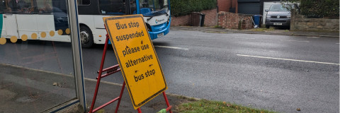 yellow bus stop closed sign with bus shelter and bus in background