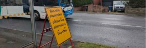 yellow bus stop closed sign with bus shelter and bus in background
